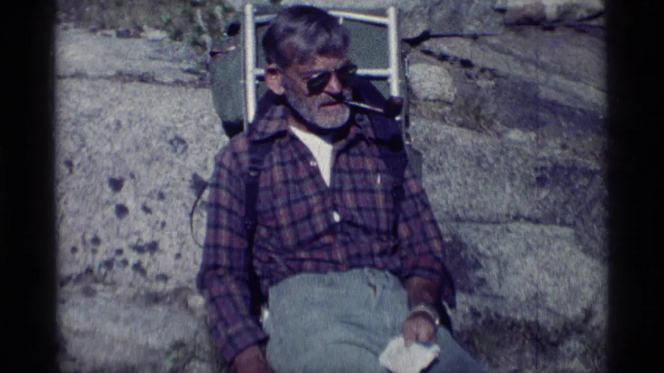 Adult hiker in sunglasses sits back on rocky ground with a pipe, framed in soft 8mm color footage from Minaret Wilderness.