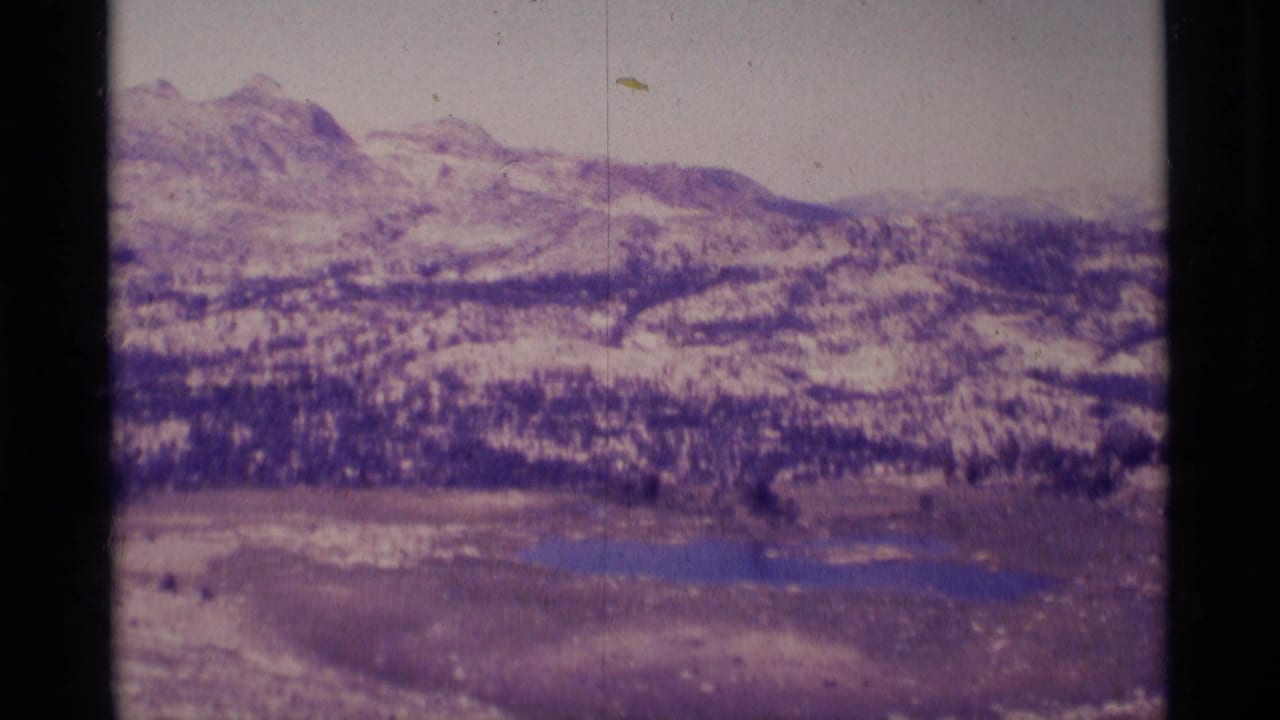 1975 8mm view of Minaret Wilderness with snow-dusted ridges, evergreen bands, meadow, and small blue lakes.