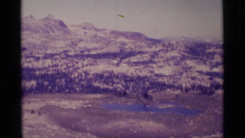 1975 8mm view of Minaret Wilderness with snow-dusted ridges, evergreen bands, meadow, and small blue lakes.