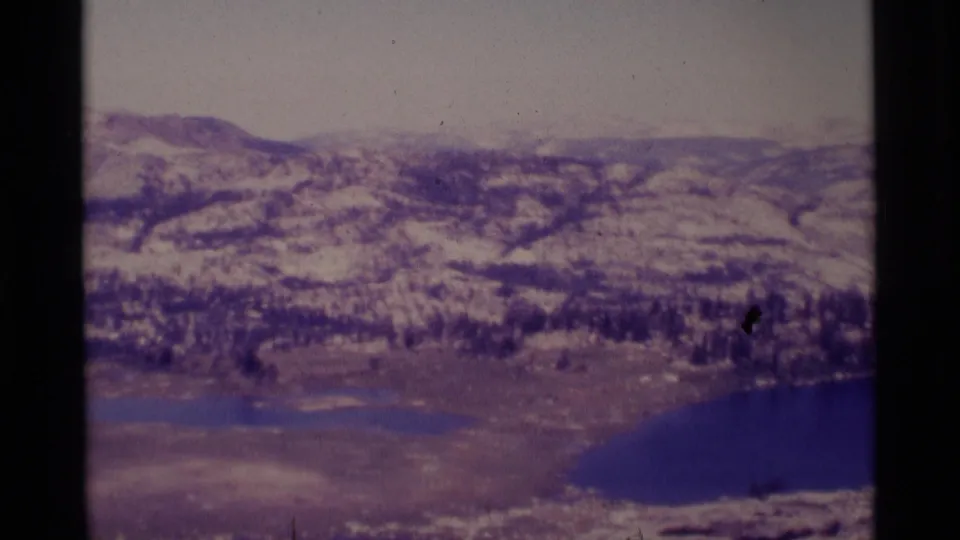 1975 8mm view across Minaret Wilderness meadow and forest toward snowy slopes, with alpine lakes at the lower edge.