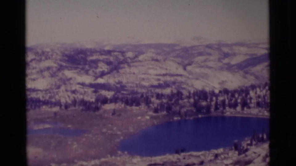 1975 8mm Minaret Wilderness frame with a prominent blue alpine lake, snowy ridges, forest bands, and muted home-movie color.