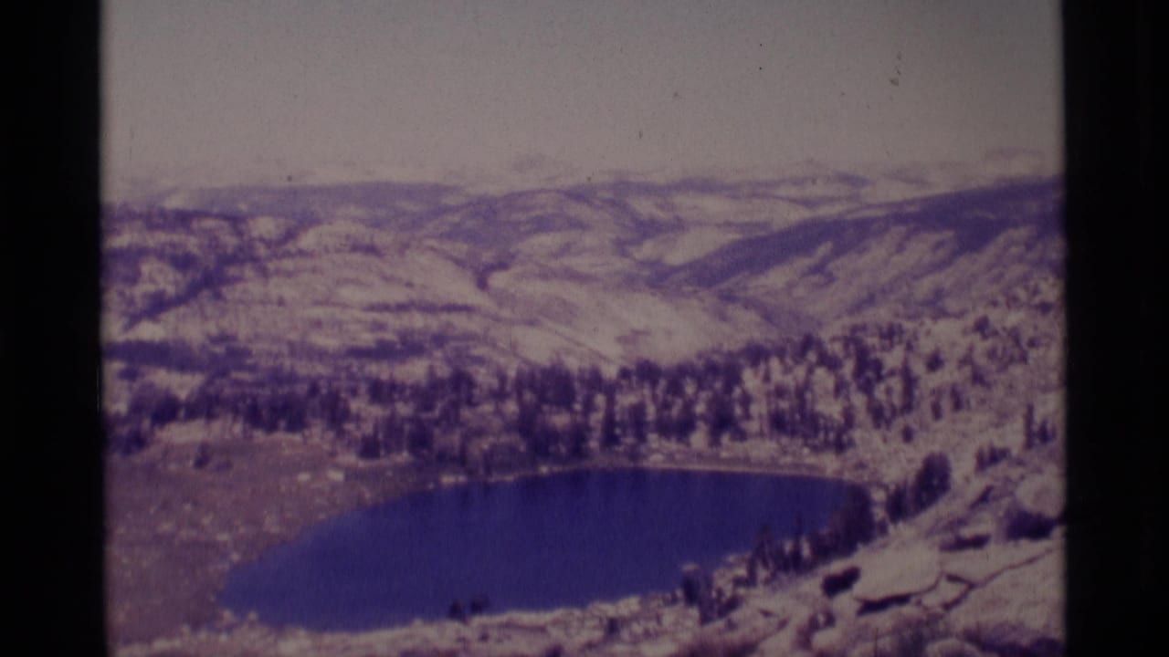 Wide overlook of a lake, trees, and snowy mountain slopes.