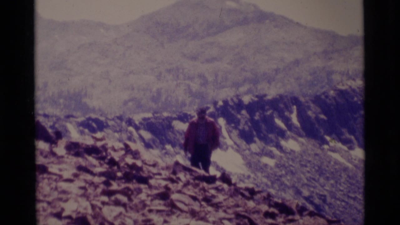 1975 8mm frame from Minaret Wilderness showing a hiker on a rocky high-country slope with mountains in the background.