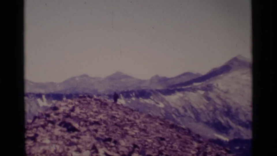 Wide 1975 Minaret Wilderness view with a small hiker on a rocky ridge and layered mountain peaks in the distance.