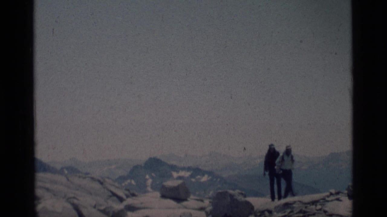 Two hikers appear near the edge of rocky high-country terrain in the Minaret Wilderness, filmed in soft 1970s 8mm color.