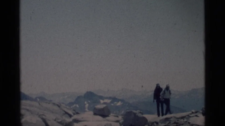 Two hikers appear near the edge of rocky high-country terrain in the Minaret Wilderness, filmed in soft 1970s 8mm color.
