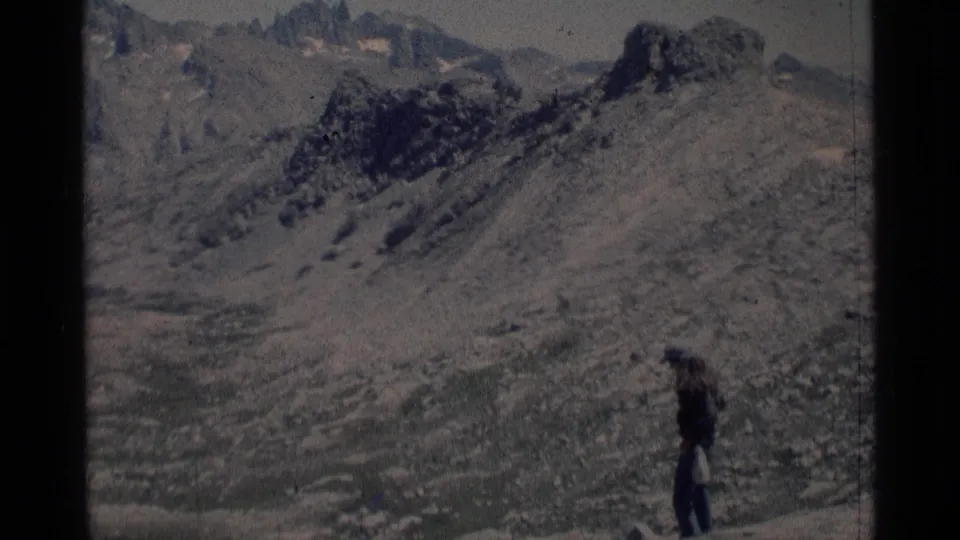 A lone hiker appears on a sloped rocky overlook in the Minaret Wilderness, with rugged high-country terrain filling the frame.