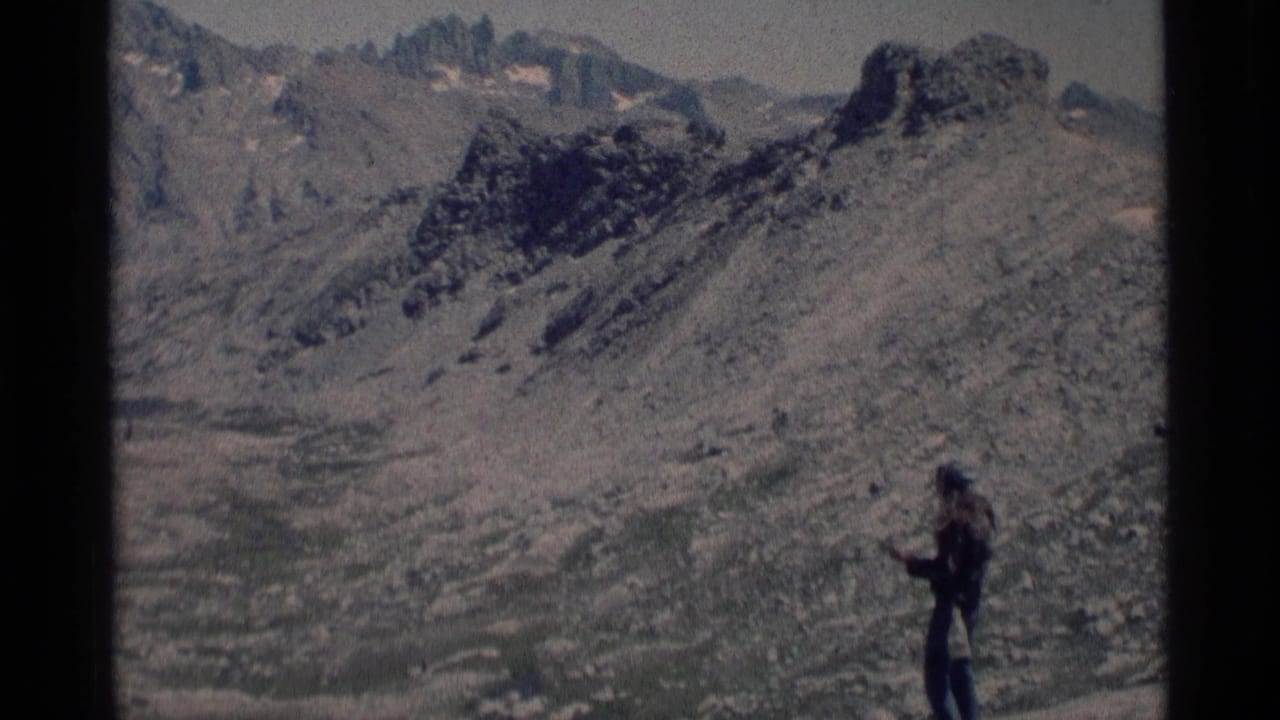 1975 8mm frame from Minaret Wilderness showing a lone hiker paused on a rocky alpine slope below jagged mountains.