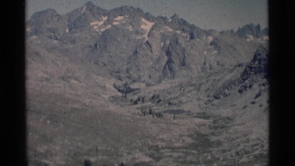 1975 8mm view of rugged Minaret Wilderness peaks with small snow patches above an open alpine valley.