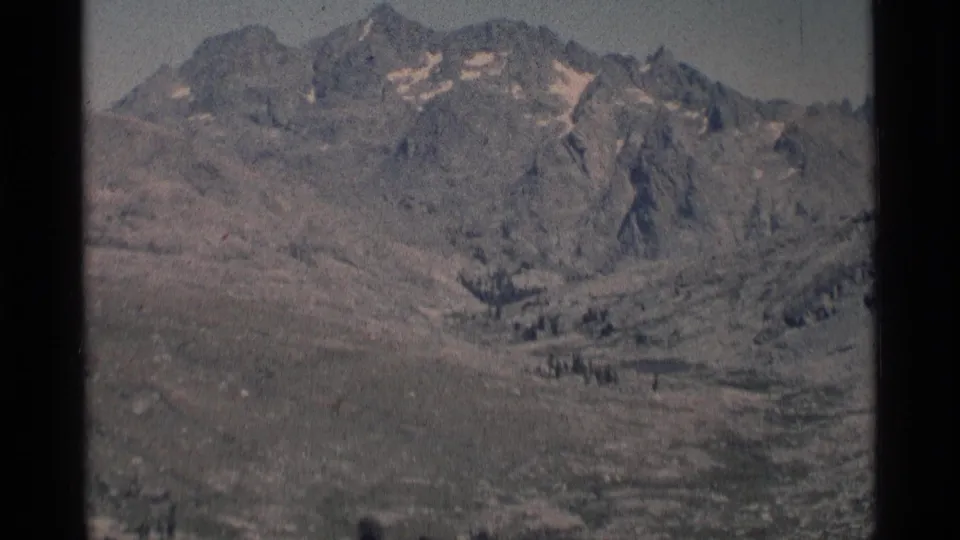 1975 home-movie frame showing rugged California wilderness peaks, valley floor, and muted 8mm color.