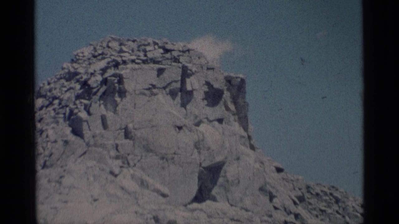 Steep fractured rock face beneath pale blue sky.