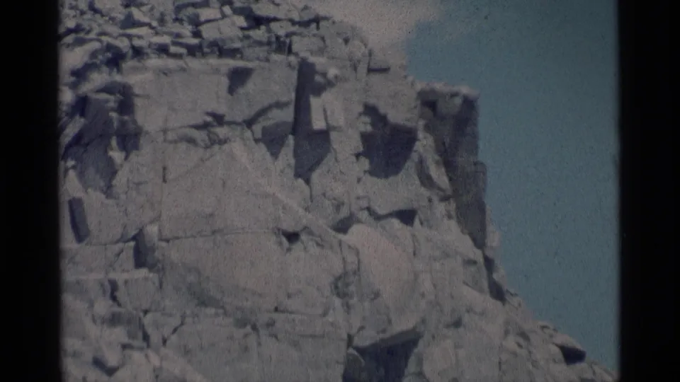 1975 8mm frame from Minaret Wilderness with a closer view of the steep broken rock wall and dark crevices against the sky.