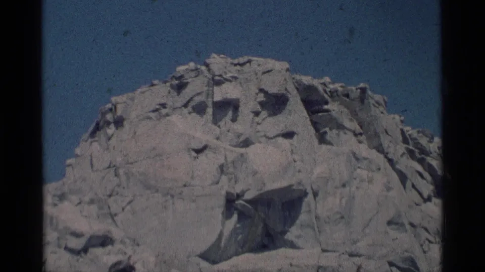 1975 California wilderness frame showing a pale granite formation against blue sky, with a visitor partly cropped at the bottom.