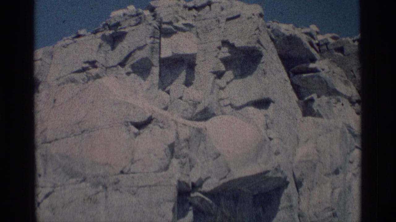1975 8mm view of a pale fractured rock face in Minaret Wilderness, California, seen below a clear blue sky.