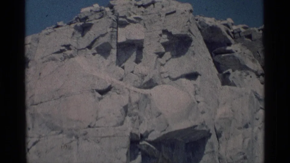 1975 8mm view of a pale fractured rock face in Minaret Wilderness, California, seen below a clear blue sky.