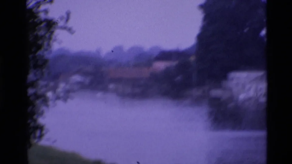 Hazy 1969 London 8mm frame looking across river water toward distant shoreline buildings and trees.