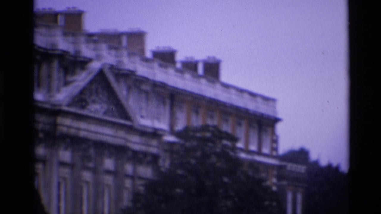 Soft 1969 London 8mm view of a grand red brick building facade, partially obscured by dark garden foliage.