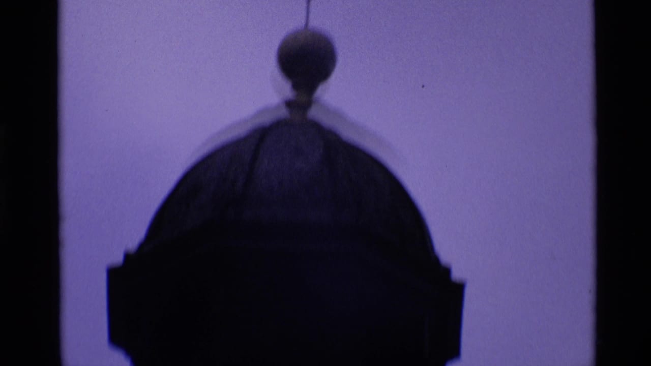 Dark silhouette of a rounded clock tower top against a pale purple sky.