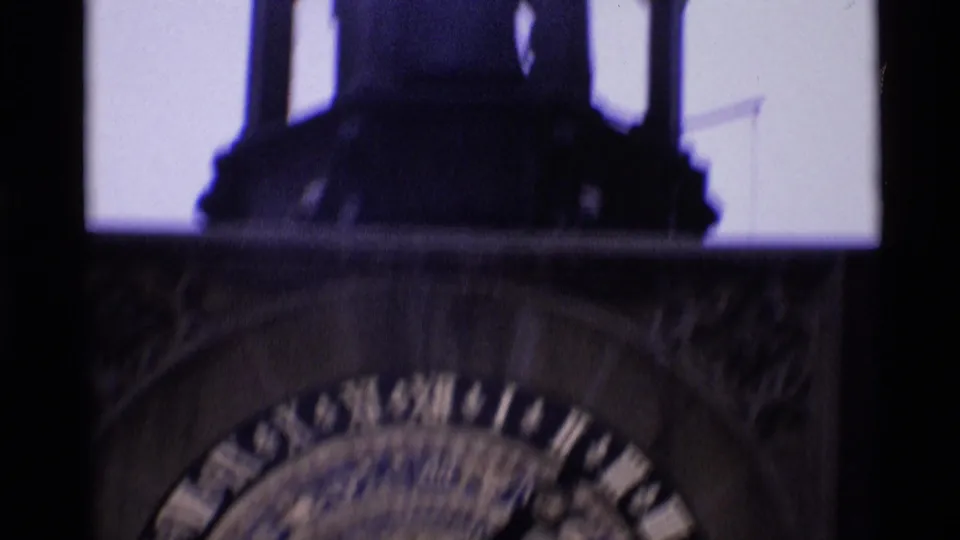 Shadowed London clock-tower detail with dark architectural framing above a blurred circular clock face.