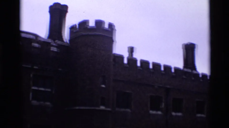 1969 London 8mm frame showing a dark crenellated exterior wall, round tower, chimneys, and pale sky.