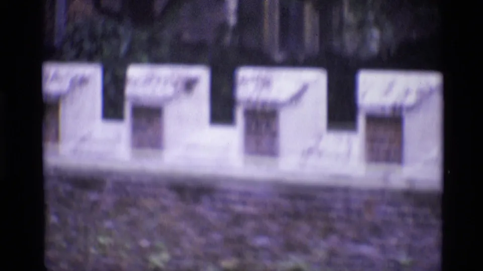 1969 London 8mm close-up of a crenellated exterior wall section with small windows, dark brick below, and soft focus.