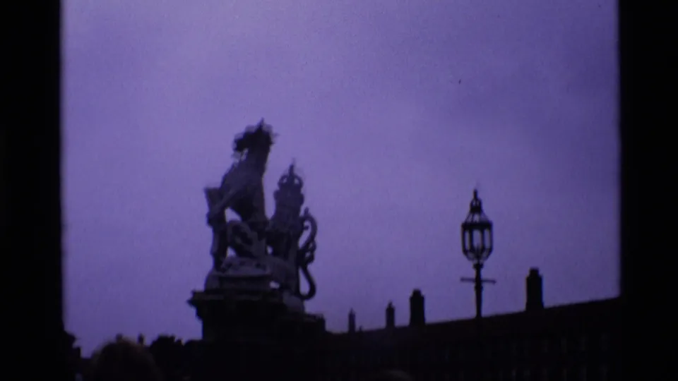 1969 London frame with a dark silhouetted statue or monument, roofline, lamp-like fixture, and purple shifted sky.