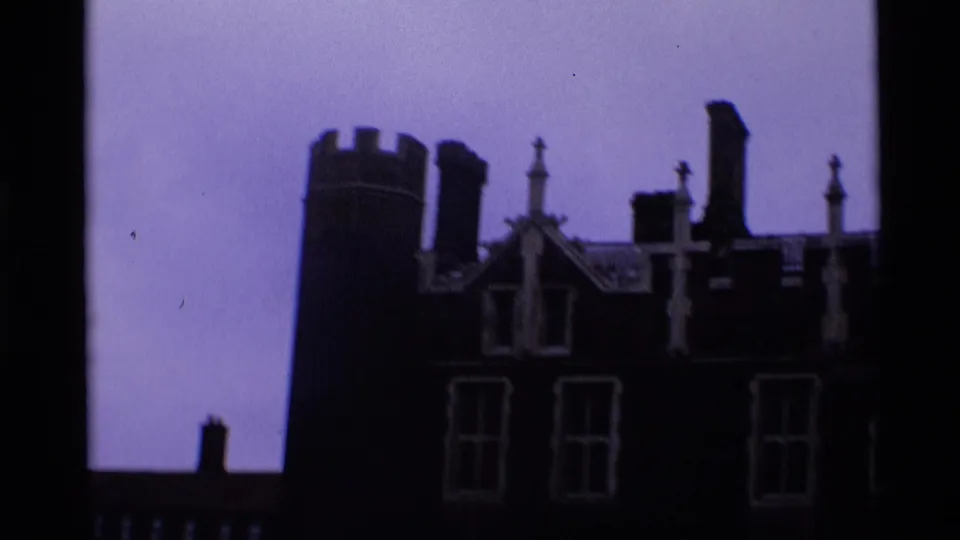 1969 London home-movie view of a dark historic building roofline with turret, chimneys, tall windows, and pale sky.