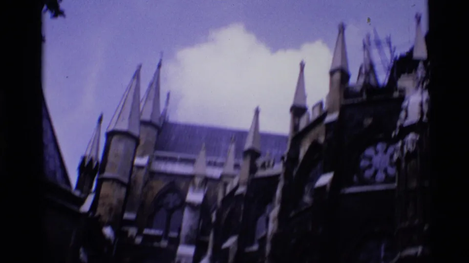 1969 London 8mm frame showing Gothic church spires and stone facade details partly obscured by trees.