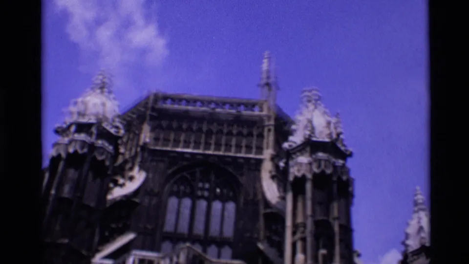 1969 London frame showing the cathedral's upper exterior, tall windows, spires, and roofline details below a blue sky.