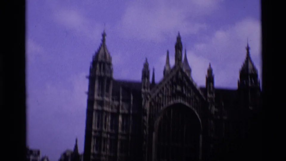 1969 London 8mm frame showing a dark Gothic landmark exterior with pointed spires and a large arched window against a purple sky.