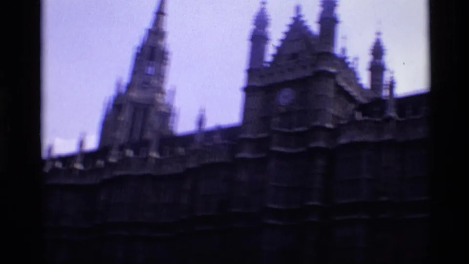 1969 London 8mm frame showing Gothic spires, roofline ornament, and dark stone exterior in soft focus beneath a pale purple sky.