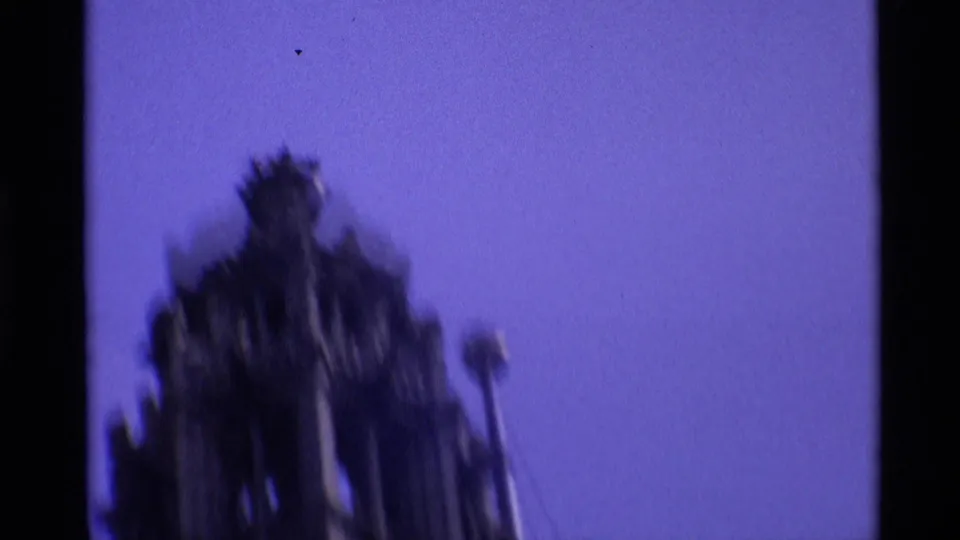 1969 London home-movie frame with a blurred upward view of a church tower or spire set against bright blue sky.