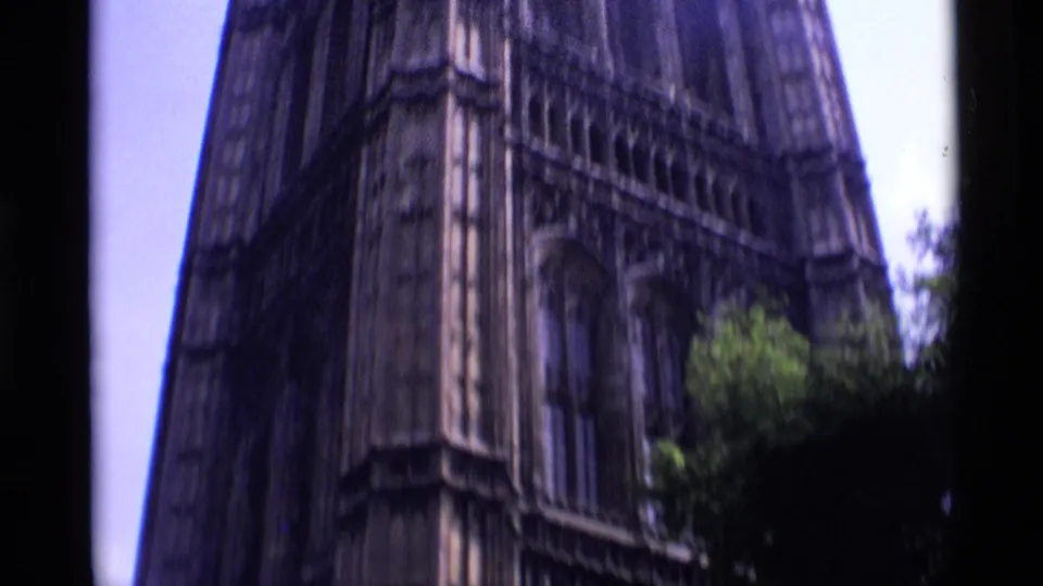1969 London 8mm frame showing a tall Gothic religious building section with narrow vertical stonework and trees at the lower edge.