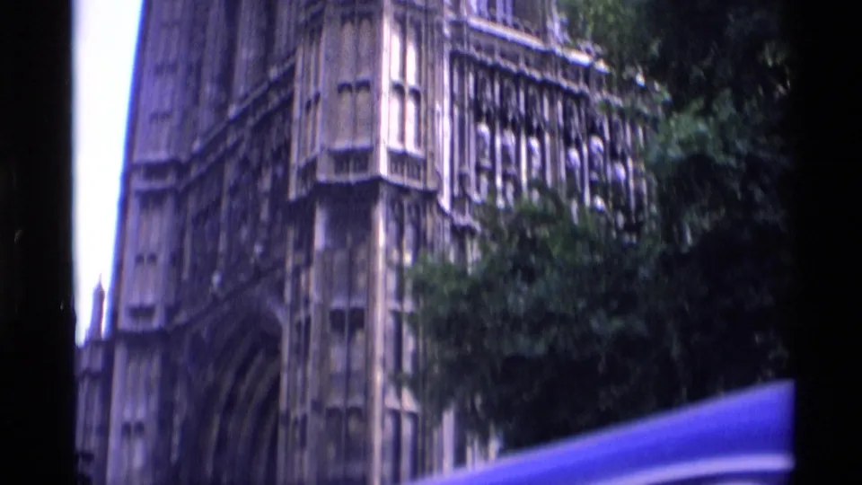 1969 London 8mm frame showing the lower portion of a Gothic church or cathedral facade, with pointed openings and leafy trees nearby.