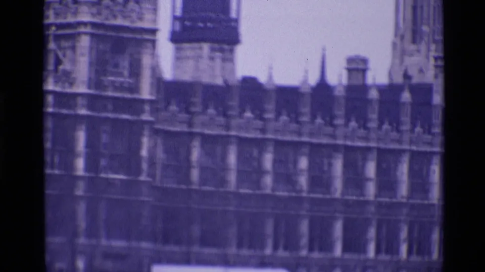 1969 London view of the Palace of Westminster facade, roofline pinnacles, and tower forms in a soft purple-tinted 8mm frame.