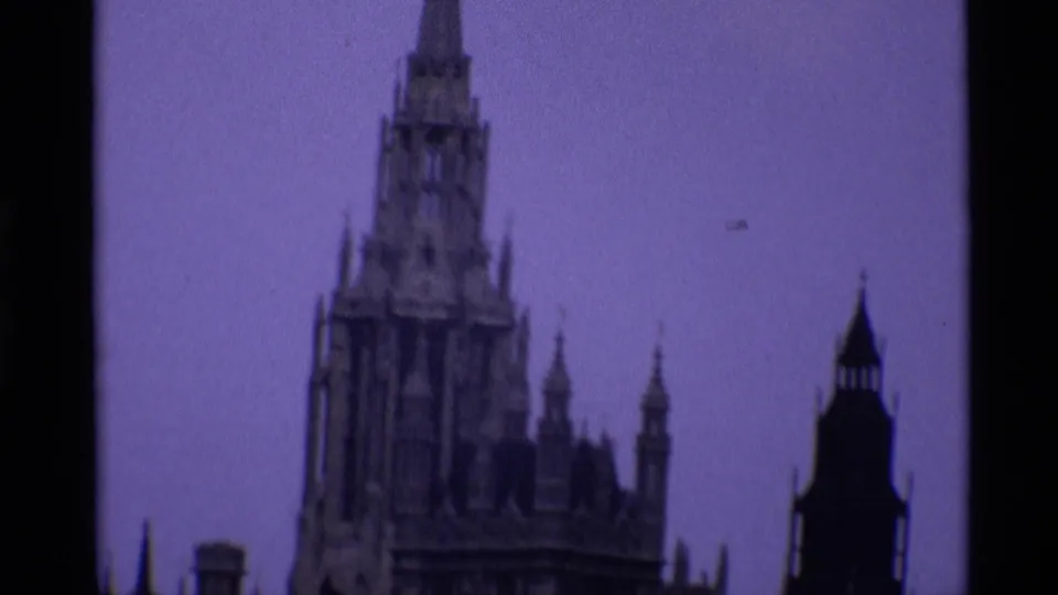 1969 London home-movie frame showing the Palace of Westminster roofline and Gothic spires with dark film edge visible.