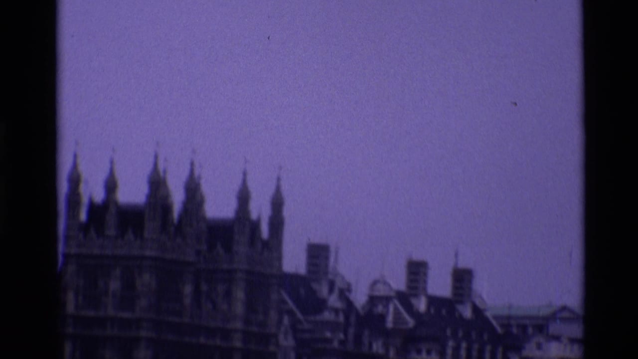 1969 London home-movie frame with Westminster's Gothic roofline and nearby rooftops seen from a distance.