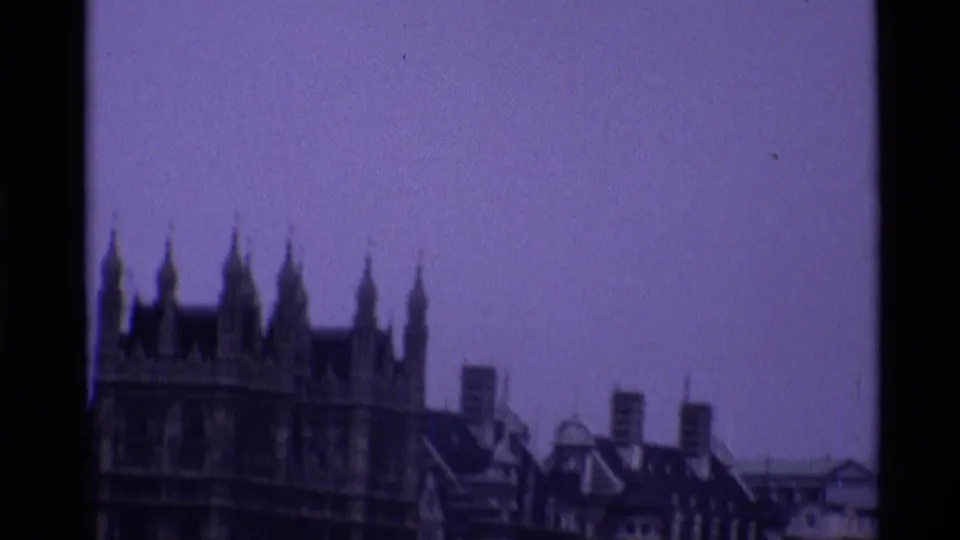 1969 London home-movie frame with Westminster's Gothic roofline and nearby rooftops seen from a distance.