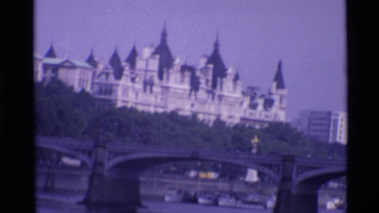 1969 London home-movie frame showing a Gothic-style building beyond a stone bridge over the River Thames.