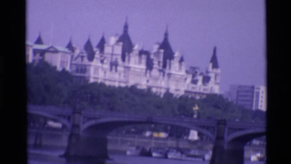 1969 London home-movie frame showing a Gothic-style building beyond a stone bridge over the River Thames.