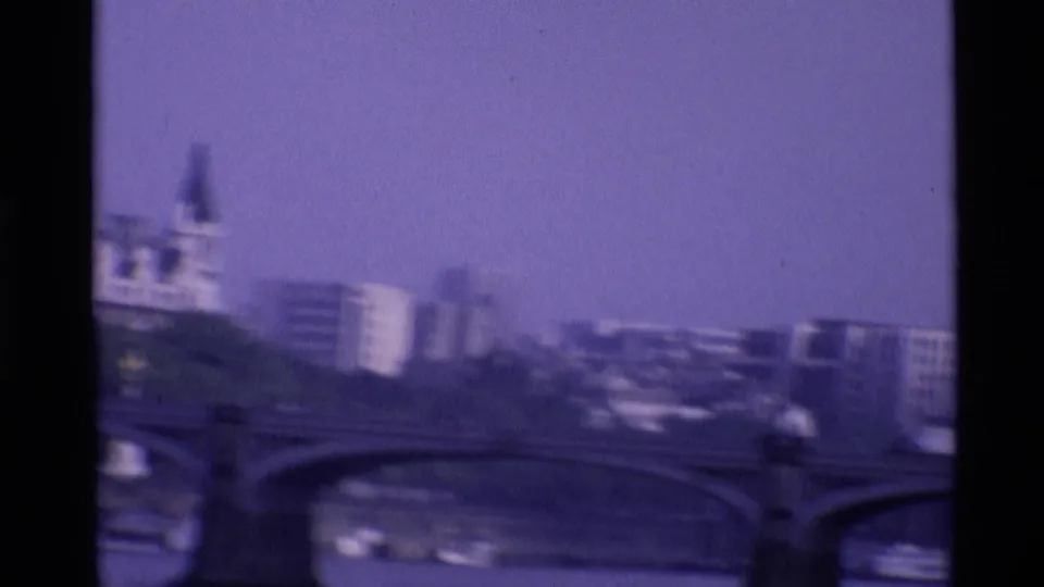 Soft 1969 London view across the Thames, with bridge arches, traffic, boats, and modern riverside buildings.