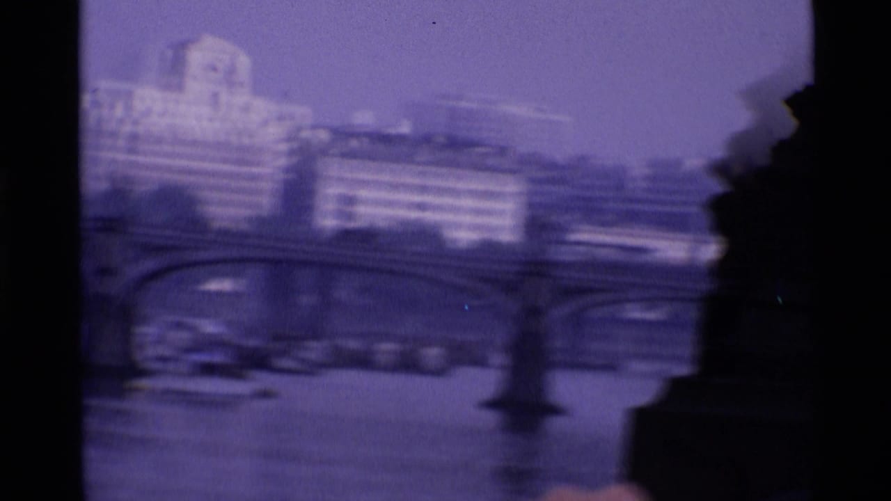 Soft, shaky riverfront view with bridge arches and distant buildings.