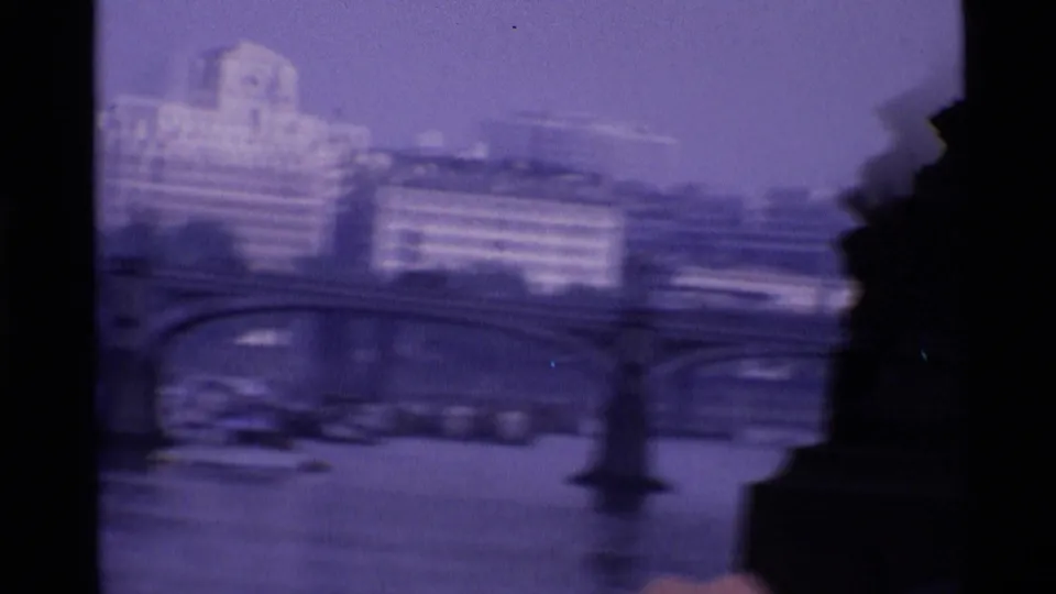 1969 London home-movie frame showing a blurred riverfront, bridge arches, and older buildings under a purple film cast.