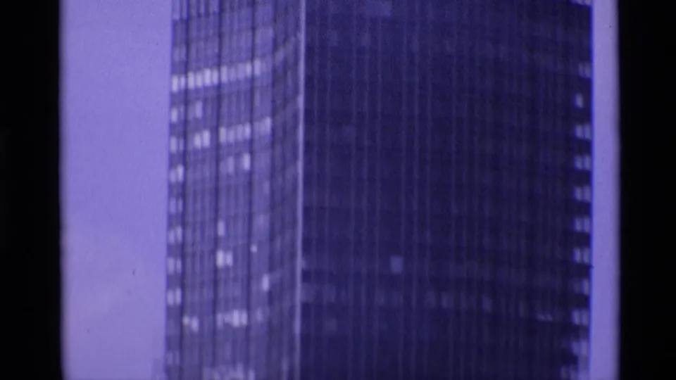 Close, soft 1969 London frame of a tall glass-and-steel skyscraper seen through purple-tinted 8mm film.