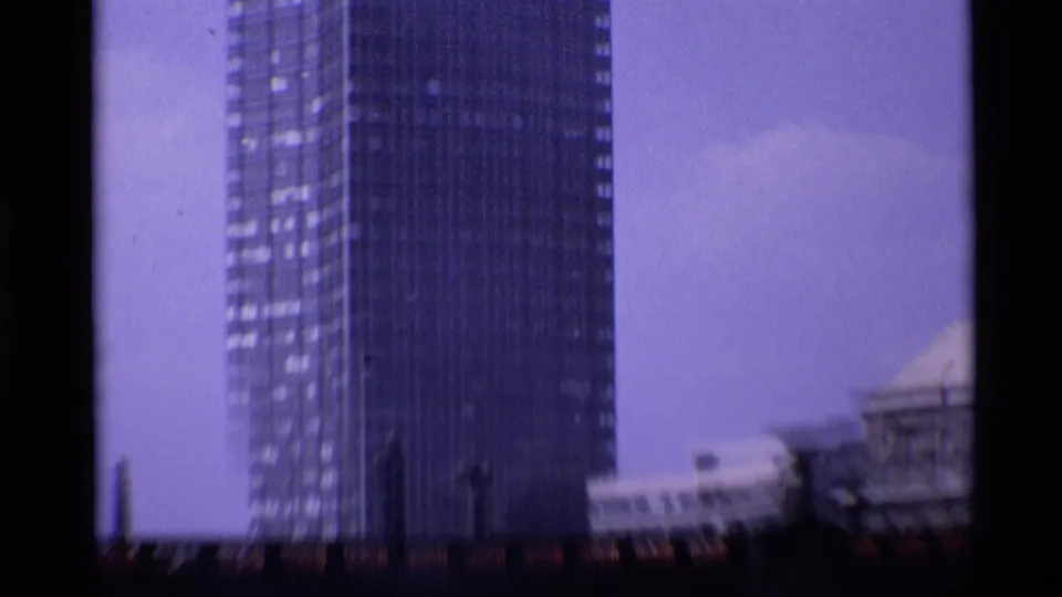 Purple-cast 8mm frame with a tall tower at left and partial older riverside architecture at right.