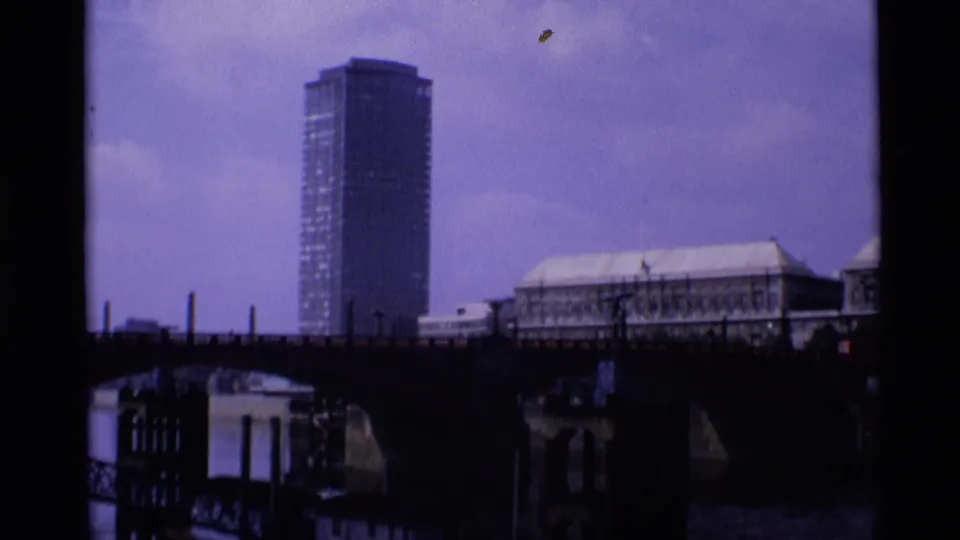 1969 London river view with a high-rise tower beyond a dark bridge and a large roofed riverside building.