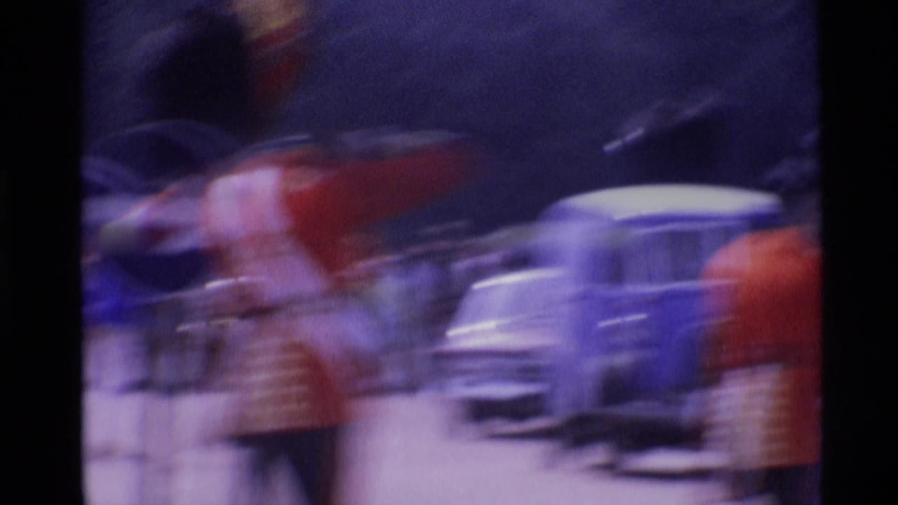 Soft, motion-blurred 1969 London home-movie frame of guards in red uniforms passing a light-colored car on a busy street.