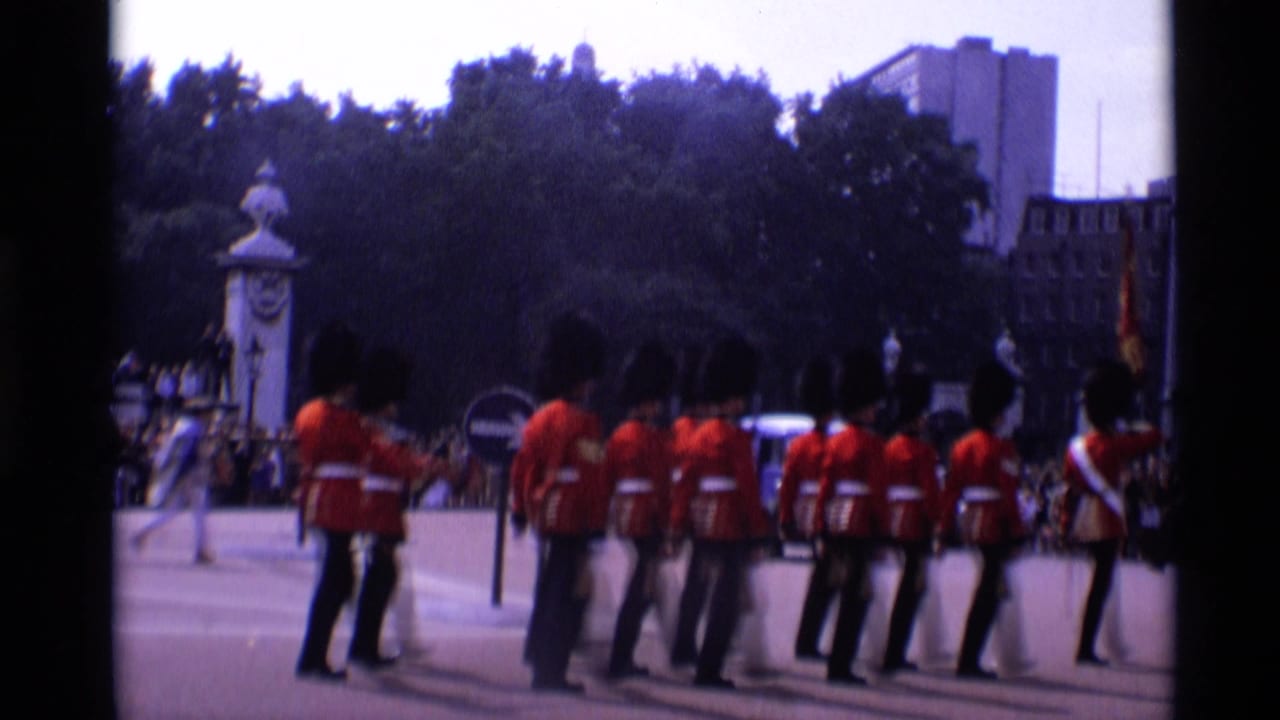 Line of guards in red uniforms standing or marching near trees and buildings.