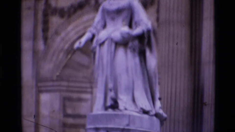 1969 London home-movie frame of a robed stone statue set against columns and ornate architectural details.