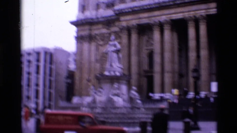 1969 London street view with a columned landmark facade, statue, red car, and pedestrians in public space.